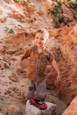 Küçük bir çocuk kumların arasında bir kayanın üzerinde duruyor.
