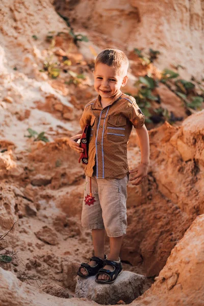 Küçük bir çocuk kumların arasında bir kayanın üzerinde duruyor.