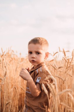A sad child stands in a field of wheat and looks ahead.