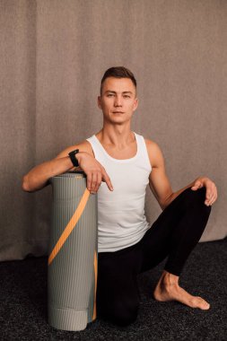 Erkek sporcu spor salonunda oturur ve elini arabaya yaslar.