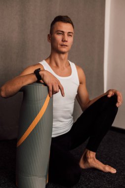 Erkek sporcu spor salonunda oturur ve elini arabaya yaslar.