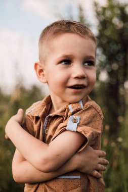 Küçük bir çocuk gülümser ve doğadaki bir parka bakar.
