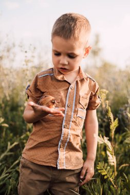 Küçük bir çocuk elinde bir salyangoz tutuyor ve dikkatlice inceliyor.