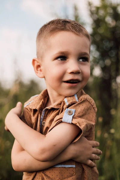 Küçük bir çocuk gülümser ve doğadaki bir parka bakar.