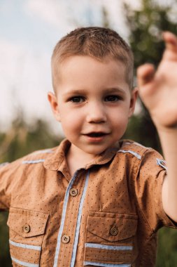 A little boy stands in nature and smiling