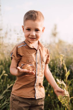 A little boy stands in the grass in nature and holds a snail in his hand