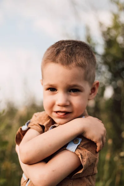 Un bambino con una camicia seria sta in piedi nella natura abbracciandosi con le mani — Foto Stock