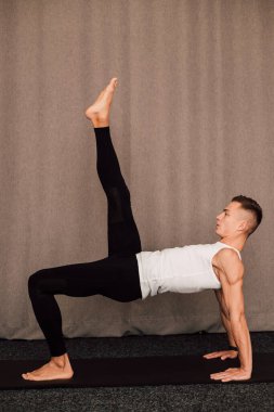 Yakışıklı bir erkek sporcu antrenman yapıyor ve bacağını kaldırıyor.