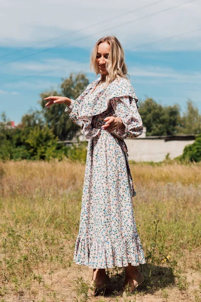 A woman in a long country dress stands in a field in the countryside — Fotografia de Stock