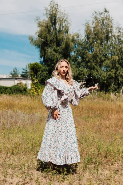 A woman in a long country dress stands in a field in the countryside — 스톡 사진