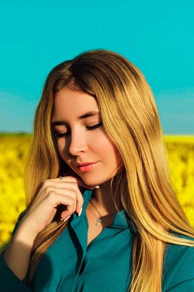 A young beautiful woman stands in a yellow rapeseed field against a blue sky — Stockfoto