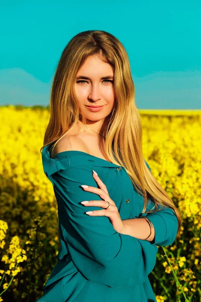 A young beautiful woman stands in a yellow rapeseed field against a blue sky — 스톡 사진