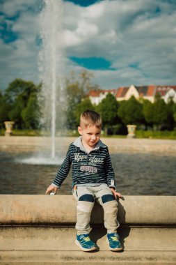 Güneşli bir günde küçük bir çocuk çeşmenin yanında oturur..