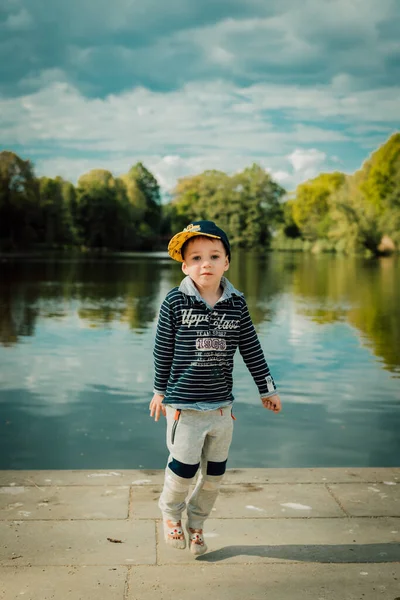 Küçük bir çocuk yazın bir parkta gölün yanında durur.