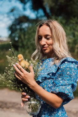Kırsal kesimde genç bir kız elinde ördek yavrusu dolu bir sepet tutuyor.