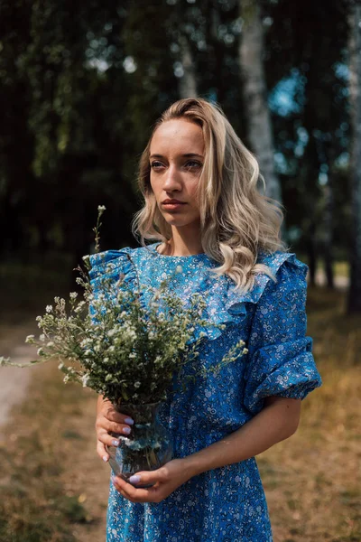 Une jeune belle femme dans une robe bleue tient des fleurs sauvages dans ses mains — Photo