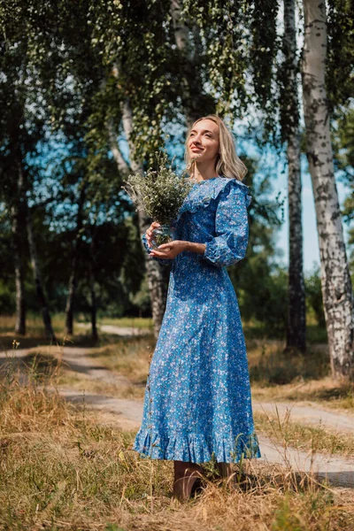 Una joven hermosa mujer en un vestido azul sostiene flores silvestres en sus manos — Foto de Stock