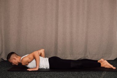 Yan görüş. Adam elleri dinlenirken yerde yatar. Sporcuların kollarındaki kaslar açıkça görülüyor.