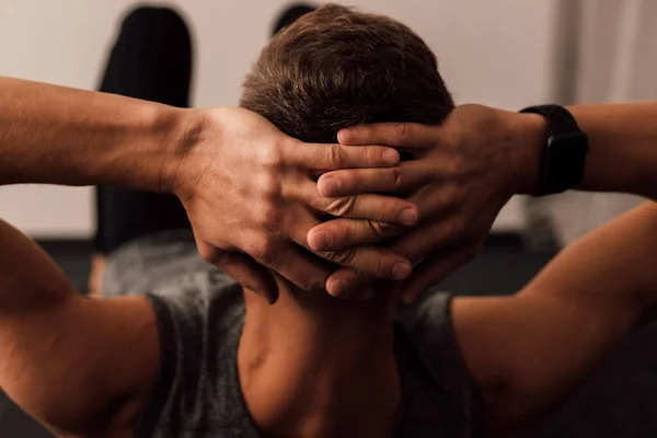 Mens hands and head close-up. A man swings his abs lying on the floor of the room. Sports at home