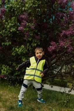Parlak yeşil yelekli küçük bir çocuk leylağın yanında eğleniyor. Yüksek kalite fotoğraf