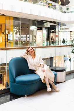 Açık renk elbiseli genç bir kadın, eline yaslanmış mavi bir kanepeye oturur. Yüksek kalite fotoğraf