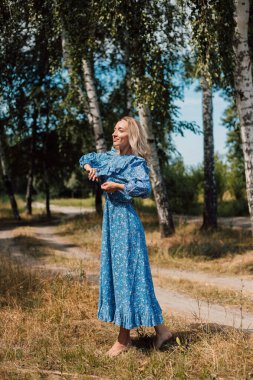 Çıplak ayaklı bir kadın. Kırsal tarzda. Arka planda Birch Grove var. Güzel sarışın.