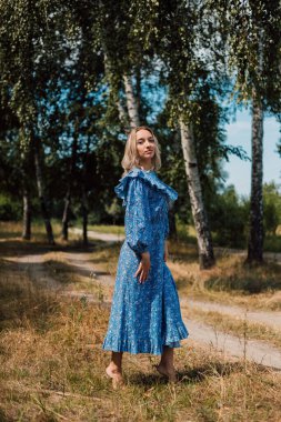 Çıplak ayaklı bir kadın. Kırsal tarzda. Arka planda Birch Grove var. Güzel sarışın.