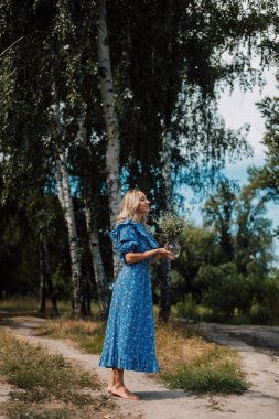 A young beautiful woman stands with her back in the woods in a long blue dress. High quality photo