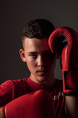 The guy clutched his red gloves tightly together and looked ahead. The guy is wearing a red T-shirt and red gloves. Dark background behind