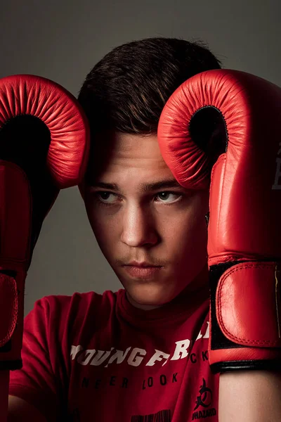 The guy pressed the gloves to his head and looked to the side with a frown. The guy is wearing a red T-shirt and red gloves. Dark background behind