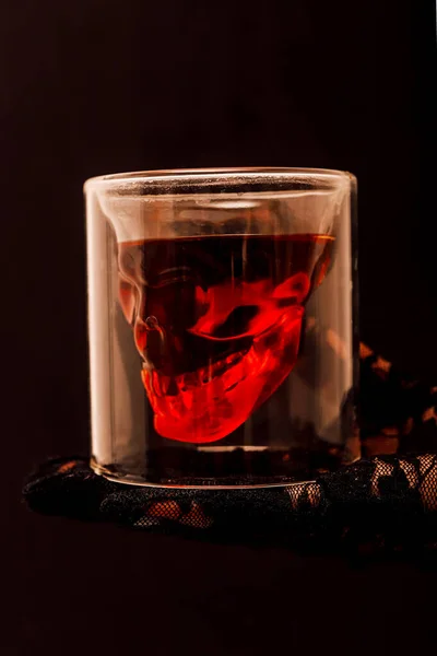 Whiskey glass with a skull on the arm on a black background. Halloween. High quality photo
