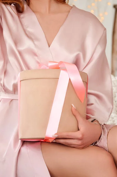 Pink gift in the hands of a young sexy girl in a bathrobe. High quality photo