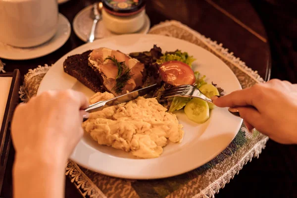 Womens hands with a fork and knife over a plate of food. High quality photo