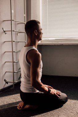 Beyaz tişörtlü genç bir adam pencerenin önünde oturarak sabah egzersizleri yapıyor. Yüksek kalite fotoğraf