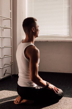 Beyaz tişörtlü genç bir adam pencerenin önünde oturarak sabah egzersizleri yapıyor. Yüksek kalite fotoğraf