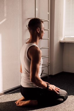 Beyaz tişörtlü genç bir adam pencerenin önünde oturarak sabah egzersizleri yapıyor. Yüksek kalite fotoğraf