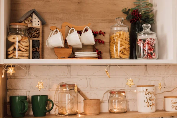 Raflarda bir sürü kap, tabak ve baharat var. Mutfak Noel çelenkleriyle, Noel ağaçlarıyla süslenmiş.