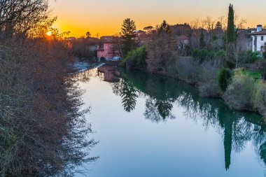 Cormons, İtalya 'da Komün, Friuli-Venezia Giulia, nehir kanalı ve ağaçlar, köyde gün batımı ve evler. 