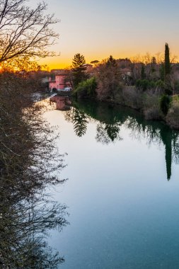 Cormons, İtalya 'da Komün, Friuli-Venezia Giulia, nehir kanalı ve ağaçlar, köyde gün batımı ve evler. 
