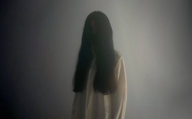 Yüzü olmayan beyaz bir Asyalı kadının hayaletli bir siluetinin bulanık görüntüsü, uzun orman saçı, perili bir şekilde ortaya çıkıyor. Yoğun bir siste