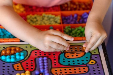 Çocuklar yakın çekim yapar. Çocuk bir mozaik toplar. Çocuk oyun sahasına mozaiğin bir parçasını yerleştirir..