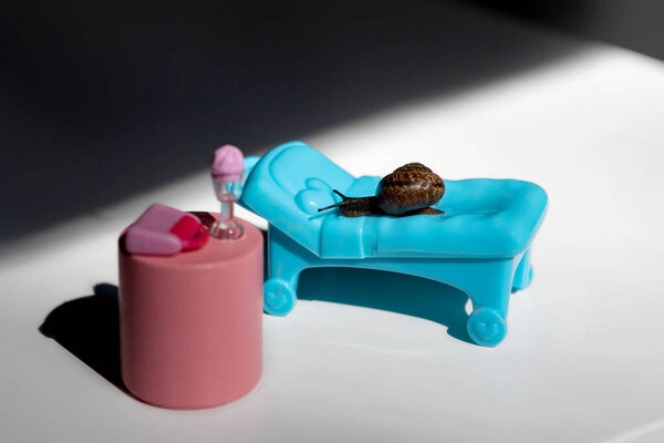 A snail in the sun on a chaise longue.A blue chaise longue and a pink cocktail table.Summer holidays on the beach