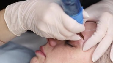 Usta, iğne dövme makinesiyle kalıcı kaş makyajı yapıyor.