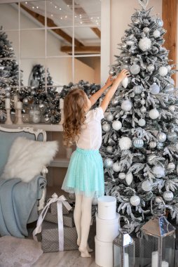 Kız arkasında duruyor ve Noel ağacını süslüyor.