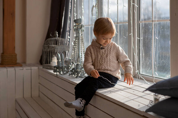 A blond-haired boy is playing near the window