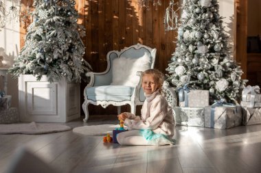 Bir kız Noel ağaçlarının arkasında yerde oynuyor.