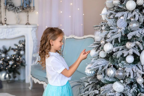 Una chica rubia busca el árbol de Navidad para colgar un juguete —  Fotos de Stock