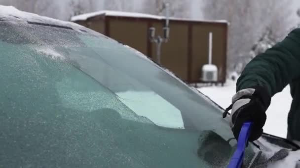 Um homem limpa o pára-brisas de um carro da neve com uma escova — Vídeo de Stock