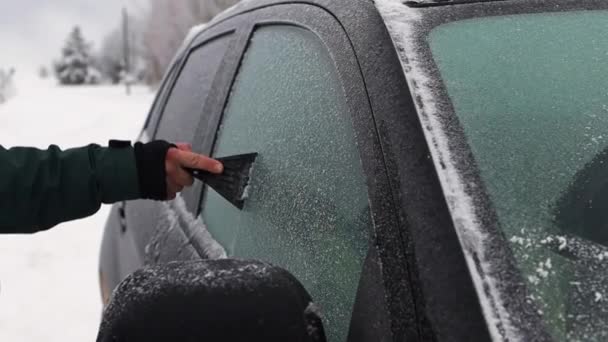 Seorang pria membersihkan gelas mobil dengan scraper dari kerak salju — Stok Video