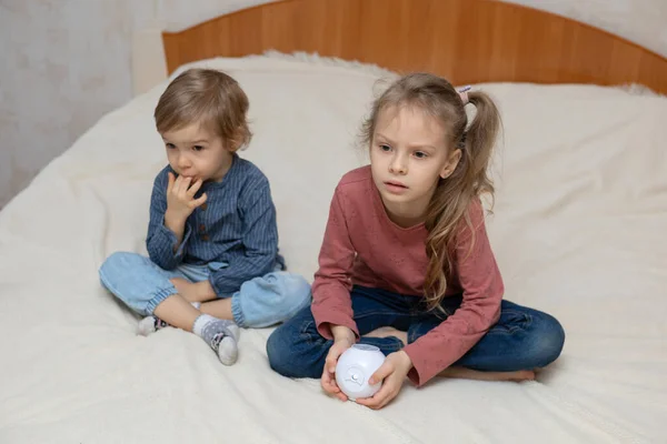 A boy and a girl are sitting on a bed with a cube-shaped projector — Foto Stock